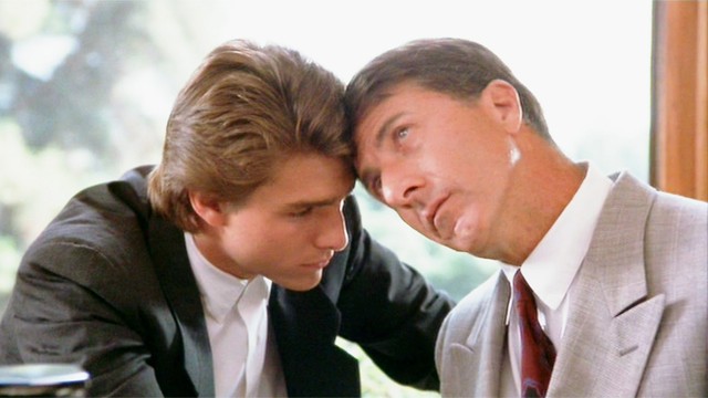 #PraCegoVer Audiodescrição resumida: Fotografia do filme “Rain Man”. No centro, há dois homens sentados com a testa encostada na testa do outro. À esquerda, o homem de pele branca e cabelos loiros; ele usa um terno preto, uma camisa branca e olha para baixo. À direita, o homem de pele branca e cabelos castanhos; ele usa um terno cinza, uma camisa branca, gravata vermelha e olha para cima.